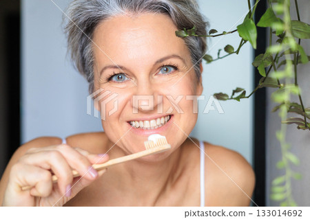 European white-skinned middle-aged woman with gray hair, smiling and brushing her teeth 133014692