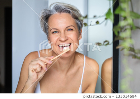 European white-skinned middle-aged woman with gray hair, smiling and brushing her teeth 133014694