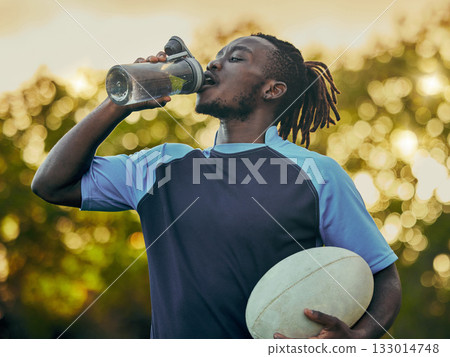 Drinking water, fitness and rugby with a sports black man outdoor for a competitive game or event. Exercise, training and health with a male athlete taking a drink from a bottle during a break 133014748