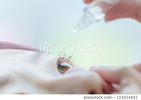 A woman putting eye drops into her eyes 133014881