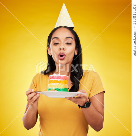 Woman, birthday cake and celebration, blow out candle with rainbow dessert isolated on yellow background. Celebrate, festive and young female, making a wish with sweet treat and party hat in studio Woman, birthday cake and celebration, blow out candle with rainbow dessert isolated on yellow background. Celebrate, festive and young female, making a wish with sweet treat and party hat in studio 133015108