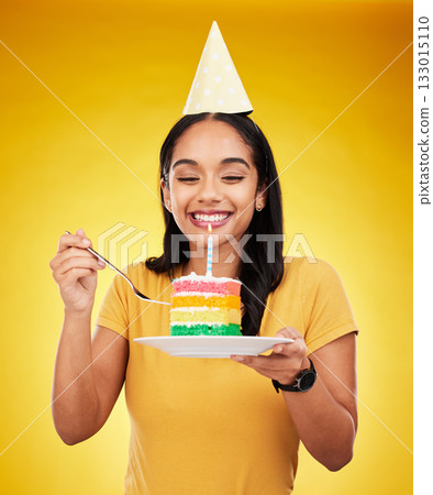 Woman is eating cake, birthday celebration and happy in portrait, rainbow dessert and candle on yellow background. Celebrate, festive and young female, excited for sweet treat and party hat in studio Woman is eating cake, birthday celebration and happy in portrait, rainbow dessert and candle on yellow background. Celebrate, festive and young female, excited for sweet treat and party hat in studio 133015110