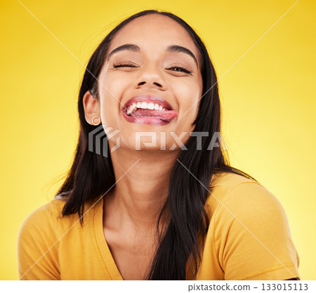 Woman, portrait smile and tongue out with silly facial expression against a yellow studio background. Happy, fun and goofy carefree female model smiling with teeth and funny face in joyful happiness Woman, portrait smile and tongue out with silly facial expression against a yellow studio background. Happy, fun and goofy carefree female model smiling with teeth and funny face in joyful happiness 133015113