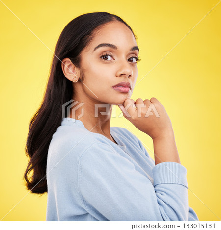 Portrait, thinking and a woman on a yellow background in studio feeling thoughtful or contemplative. Face, idea and an attractive young female standing hand on chin while contemplating a thought 133015131