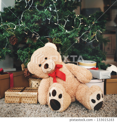 Christmas, gift and festive with a teddy bear by a tree, ready for celebration during the holiday season. December, event and a stuffed animal sitting in the living room of an apartment as a present 133015283