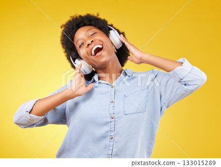 Black woman, headphones and freedom, listening to music and happiness with dance on yellow studio background. Happy female, carefree and sing along to radio, audio streaming with fun and technology 133015289