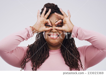 Portrait, funny face and finger mask with a black woman laughing in studio on a white background for humor. Comic, comedy and hands as glasses with a playful young female person joking or having fun 133015369
