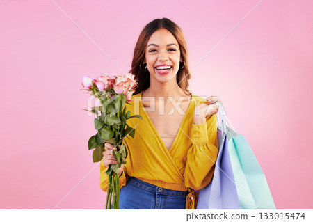 Happy, shopping bags and flowers with portrait of woman in studio for retail, birthday and spring. Event, party and smile with female and roses on pink background for sale, discount and romance 133015474