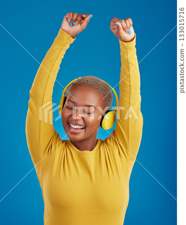 Black woman with headphones, dance and listening to music with rhythm and fun with freedom on blue background. Happy female with arms raised, streaming radio with dancing and carefree in studio Black woman with headphones, dance and listening to music with rhythm and fun with freedom on blue background. Happy female with arms raised, streaming radio with dancing and carefree in studio 133015716