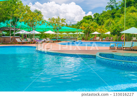 sun umbrellas and beds by swimming pool at luxury resort in nature in summer. Landscape with outdoor pool with blue water in spa hotel. Vacation and relaxation. Destination for tourism 133016227