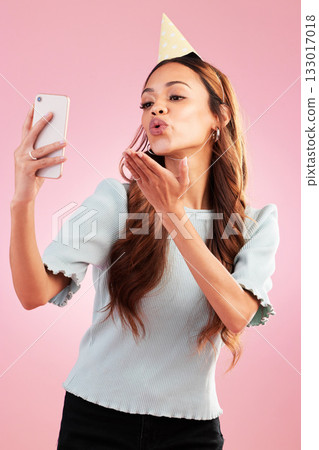 Selfie, birthday party and kiss of woman in studio isolated on a pink background. Air kissing, profile picture and mixed race female taking photo for happy memory, social media or special celebration 133017018