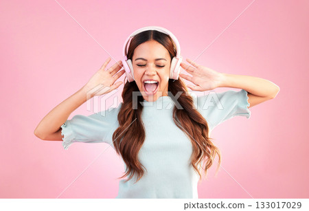 Music headphones, singing and woman dance in studio isolated on a pink background. Singer, dancing and happy mixed race female streaming, enjoying and listening to audio, sound track or radio podcast 133017029