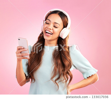 Phone, music headphones and woman singing in studio isolated on a pink background. Cellphone, radio singer and happy female with mobile streaming, laughing and listening to audio, sound or podcast. 133017036