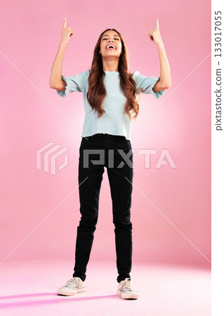 Pointing, mockup and woman in studio on pink background with happy, smile and excited for discount news. Advertising, hands and girl looking up for product placement, promotion and deal announcement 133017055