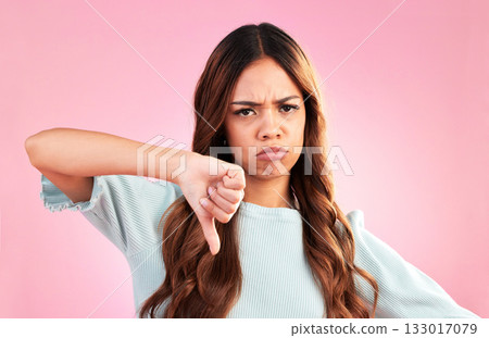 Upset, thumbs down and portrait of a female in a studio with a sad, moody or disappointed face. Loser, unhappy and young woman model posing with a angry hand gesture isolated by a pink background. Upset, thumbs down and portrait of a female in a studio with a sad, moody or disappointed face. Loser, unhappy and young woman model posing with a angry hand gesture isolated by a pink background. 133017079