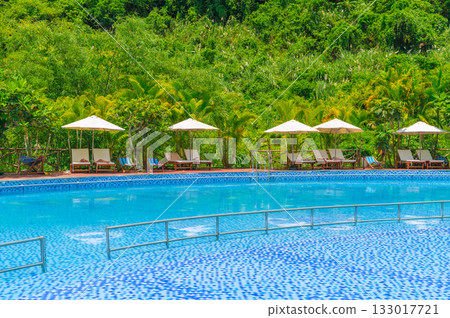 sun umbrellas and beds by swimming pool at a luxury resort in nature in summer. Landscape with outdoor pool with blue water in hotel 133017721