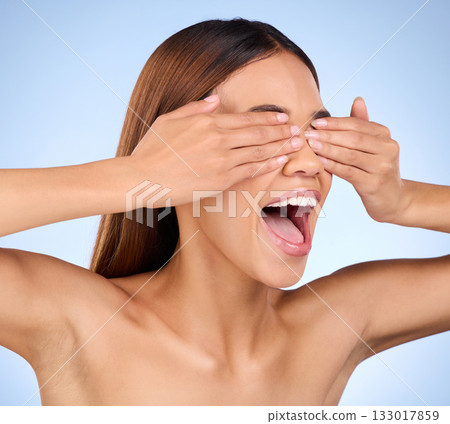 Excited, skincare and woman cover eyes, cosmetics and happiness against a blue studio background. Female, surprise and lady with hands on face, shock and wow with dermatology, treatment and soft skin 133017859