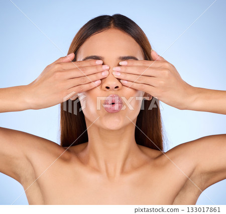 Beauty, skincare and woman cover eyes, dermatology and treatment against a blue studio background. Female, cosmetics and lady hands on face, morning routine and grooming with surprise and soft skin Beauty, skincare and woman cover eyes, dermatology and treatment against a blue studio background. Female, cosmetics and lady hands on face, morning routine and grooming with surprise and soft skin 133017861