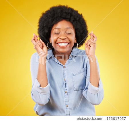 Happy, smile and fingers crossed by black woman in studio for wish, hope and good luck against yellow background. Eyes closed, hand and emoji by excited female waiting, optimistic and hopeful gesture 133017957