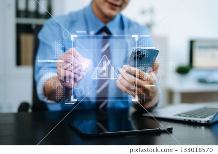 Businessman holding smartphone with digital alert icon. Concept of cyber risk, security warning, data protection, and tech threats 133018570