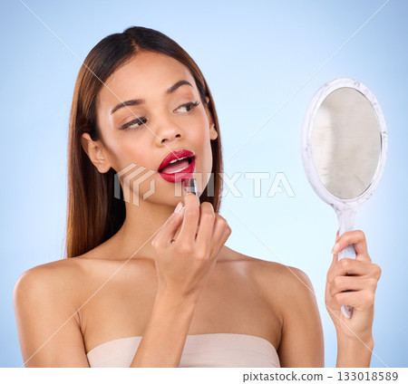 Beauty, woman and red lipstick or makeup with mirror in hand for face cosmetic product in studio. Aesthetic female model on a blue background with color application on lips for shine and self care Beauty, woman and red lipstick or makeup with mirror in hand for face cosmetic product in studio. Aesthetic female model on a blue background with color application on lips for shine and self care 133018589