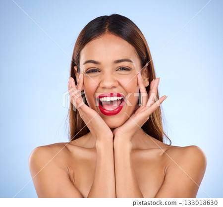 Makeup, hands on face and red lipstick portrait with beauty cosmetics in studio. Excited aesthetic female model on blue background for self care, facial glow and shine or color for skin and wellness Makeup, hands on face and red lipstick portrait with beauty cosmetics in studio. Excited aesthetic female model on blue background for self care, facial glow and shine or color for skin and wellness 133018630