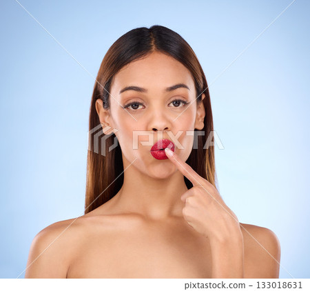 Beauty, woman and red lipstick makeup portrait with cosmetics on face in studio. Aesthetic female model with finger on lips on a blue background for self care, facial glow and shine or color for skin Beauty, woman and red lipstick makeup portrait with cosmetics on face in studio. Aesthetic female model with finger on lips on a blue background for self care, facial glow and shine or color for skin 133018631