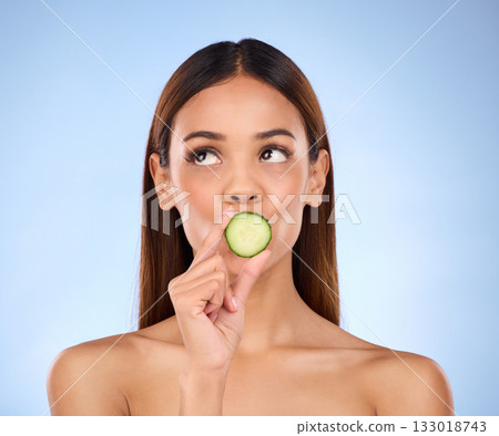 Cucumber, woman and skincare face portrait with beauty and dermatology cosmetics. Female model on a blue background thinking about self care, facial glow and healthy fruit for natural skin in studio Cucumber, woman and skincare face portrait with beauty and dermatology cosmetics. Female model on a blue background thinking about self care, facial glow and healthy fruit for natural skin in studio 133018743