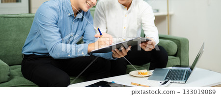 Two Asian businessmen smiling while signing a contract on clipboard, symbolizing business cooperation, teamwork Two Asian businessmen smiling while signing a contract on clipboard, symbolizing business cooperation, teamwork 133019089