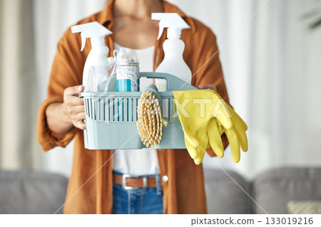 Hands, housekeeper and woman maid cleaning home with equipment, housework and person for hygiene clean house. Maintenance, service and basket of disinfectant product by worker in living room 133019216