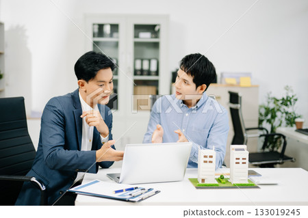 Two businessmen discuss and sign a real estate contract with housing models on a desk for concepts of property, investment 133019245