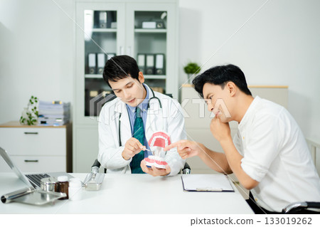 Dentist explaining dental care to male patient using a tooth model. Health consultation, oral hygiene, and professional support 133019262