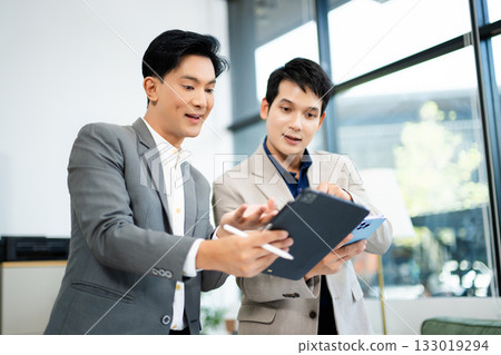 Two Asian businessmen using tablet and smartphone for project planning in a modern office. Two Asian businessmen using tablet and smartphone for project planning in a modern office. 133019294