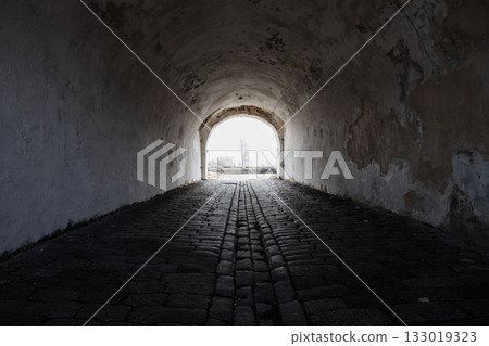An empty ancient dark tunnel with bright glowing end, abstract photo background 133019323