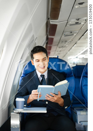 Young Asian executive excels in first class, multitasking with digital tablet, laptop and smartphone. Travel in style, work with grace. 133019400