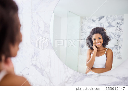 Model, face and happy with skincare in mirror at apartment for wellness and healthy glow. Woman, beauty and glow for happiness in the morning with dermatology in the bathroom at hotel for self care. 133019447