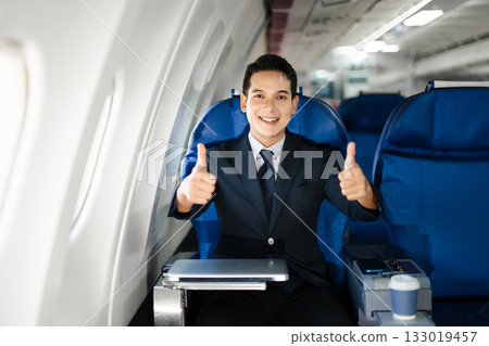 Smiling businessman in a suit giving a thumbs up while seated in first class, symbolizing success, confidence, and luxury air travel for business professionals. Smiling businessman in a suit giving a thumbs up while seated in first class, symbolizing success, confidence, and luxury air travel for business professionals. 133019457