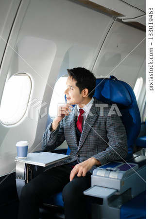 Confident businessman in first class looking out the airplane window, capturing luxury travel, success, and the modern lifestyle of business professionals. Confident businessman in first class looking out the airplane window, capturing luxury travel, success, and the modern lifestyle of business professionals. 133019463