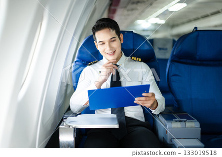 Confident airline pilot in uniform reviewing documents in airplane cabin, perfect for aviation, travel, and business lifestyle concepts. 133019518