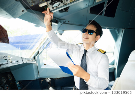 Professional airline pilot in uniform inspecting cockpit control panels during safety checks, ideal for aviation, travel, and airline safety themes. 133019565
