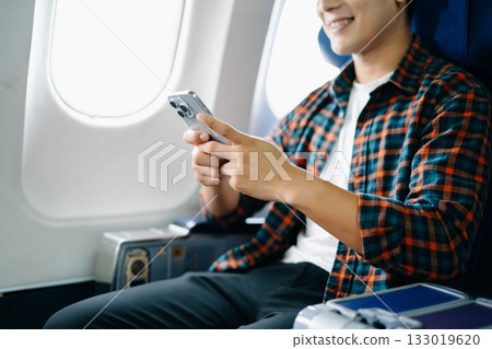 Traveler enjoys a relaxing flight. Young man on a business trip or vacation, looking out the airplane window with a smile. Traveler enjoys a relaxing flight. Young man on a business trip or vacation, looking out the airplane window with a smile. 133019620