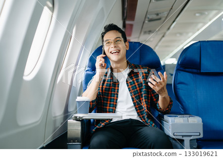 Happy traveler using modern tablet tech on a plane. Digital work, screen entertainment, or connecting with mobile internet on a business trip/journey. Happy traveler using modern tablet tech on a plane. Digital work, screen entertainment, or connecting with mobile internet on a business trip/journey. 133019621