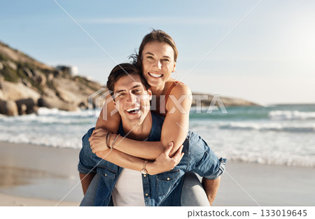 Young couple, portrait and piggyback at beach in summer sunshine with love, romance and bonding with travel. Man, woman and happy with hug, ocean waves and smile in nature, outdoor and vacation 133019645