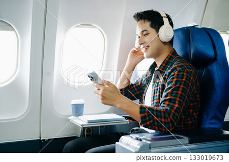 Happy man in a plane seat. Diverse travel series: work, talk, call, listen, read, stress, and joy on a long flight. Tech, mobile, and view are key parts of the trip. 133019673