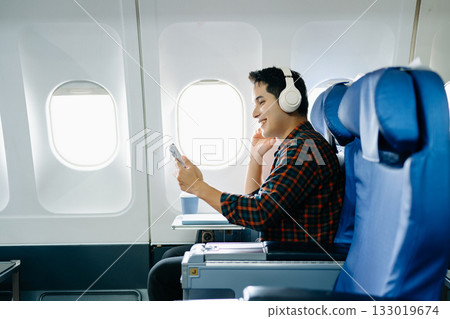 Happy man in a plane seat. Diverse travel series: work, talk, call, listen, read, stress, and joy on a long flight. Tech, mobile, and view are key parts of the trip. Happy man in a plane seat. Diverse travel series: work, talk, call, listen, read, stress, and joy on a long flight. Tech, mobile, and view are key parts of the trip. 133019674