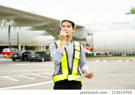 Ground crew engineer in safety vest and helmet giving thumbs up near airplane, ideal for aviation, safety, 133019709