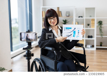 Caucasian woman in professional office showing financial chart during remote video blogging session. 133019905