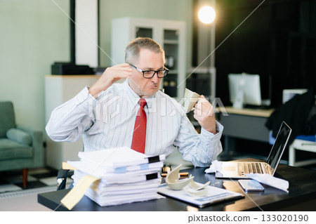 Angry and irritated Mature Businessman sitting in the office of laptop with his keyboard tired from work. Overwork, stress 133020190