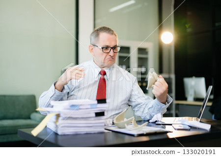 Angry and irritated Mature Businessman sitting in the office of laptop with his keyboard tired from work. Overwork, stress Angry and irritated Mature Businessman sitting in the office of laptop with his keyboard tired from work. Overwork, stress 133020191