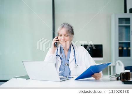 Beautiful physician doctor sit on table in office hospital. Attractive therapist female practitioner pharmacist smile and use tablet and laptop Beautiful physician doctor sit on table in office hospital. Attractive therapist female practitioner pharmacist smile and use tablet and laptop 133020388